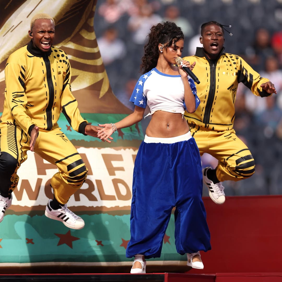 Tyla singing on stage at the 2026 FIFA World Cup opening ceremony flanked by background dancers in gold and black tracksuits.