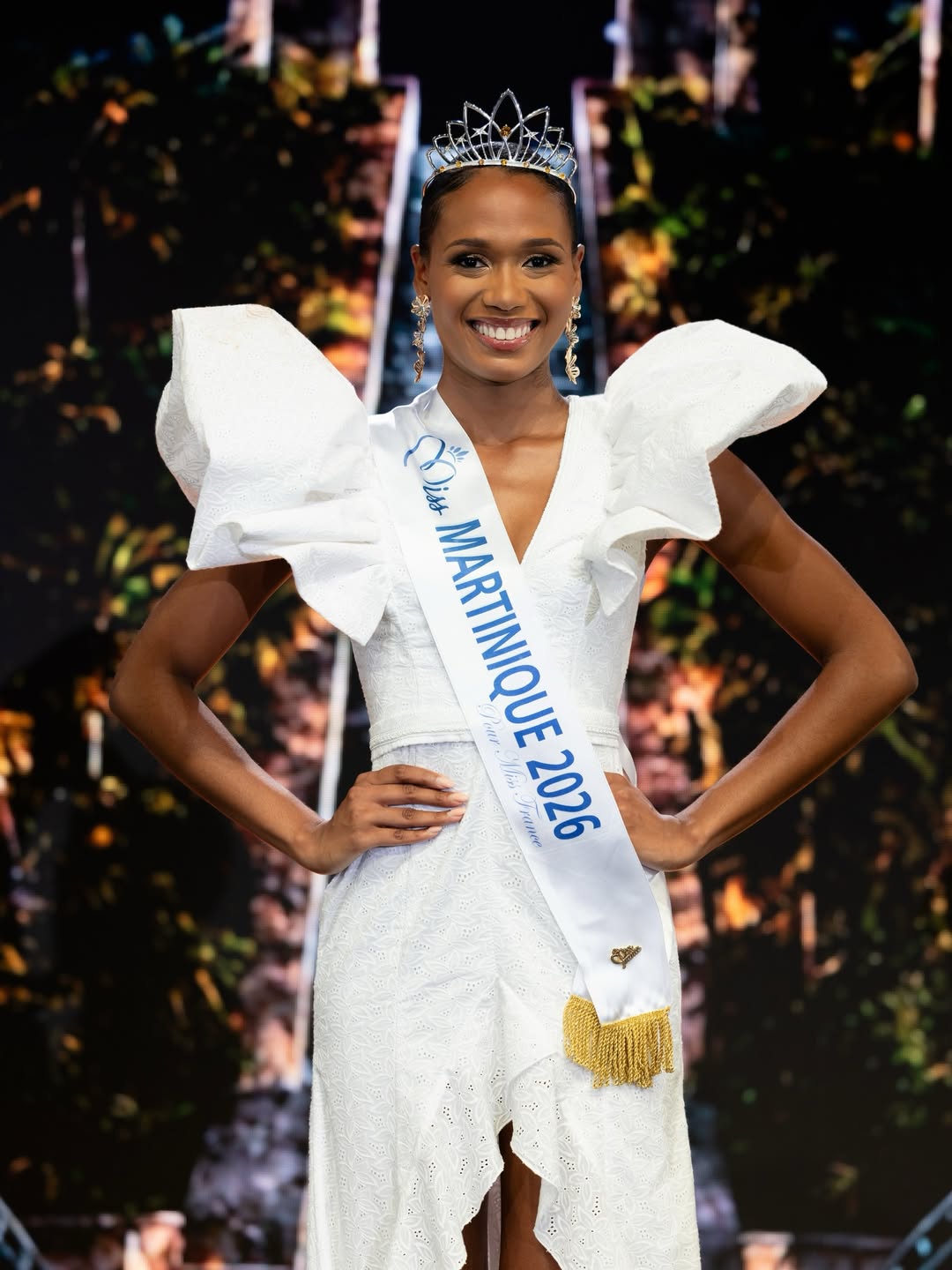 Maureen-Alycia Lucéa-Merlin wearing the Miss Martinique 2026 sash, crown, and gold drop earrings with her hands on her hips.
