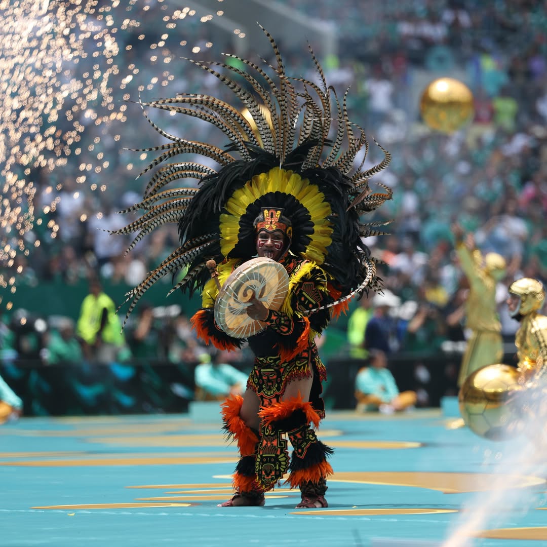 A performer in a traditional Mexican feathered headdress holding a drum during the opening ceremony.