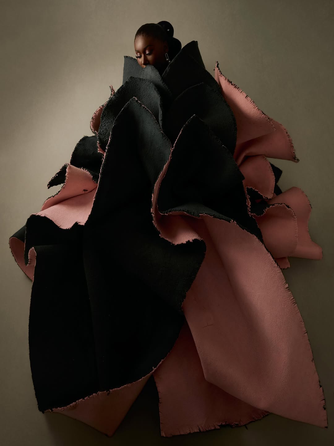 Nelly Mbonu wearing her second birthday look designed by Josiphiah Michael, showcasing a structured dress featuring cascading, oversized charcoal-black fabric layers that reveal a dusty-pink lining underneath.