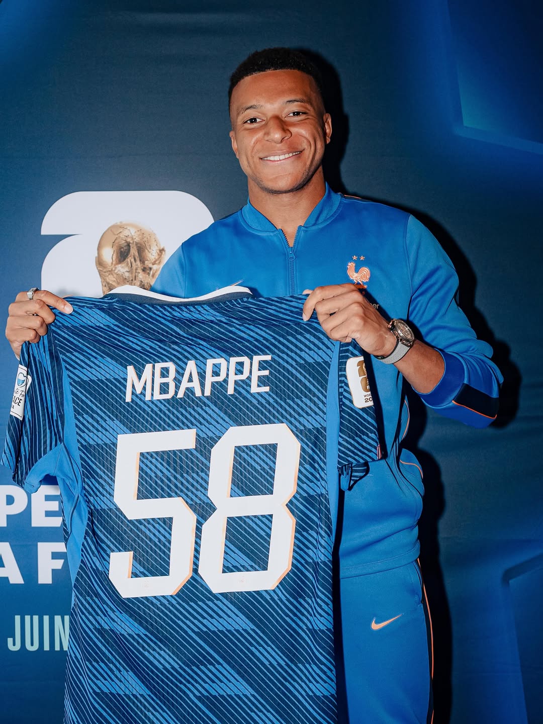 Kylian Mbappe proudly holding up a blue France football jersey printed with his name and the record number 58.