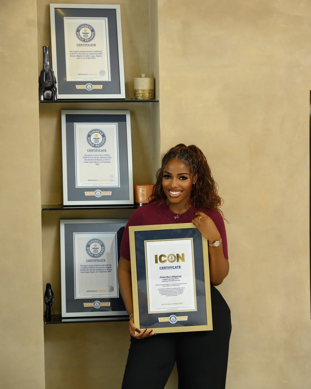 Triple world record holder Hilda Baci smiling while holding her framed Guinness World Records Icon certificate in front of a shelf displaying her other official plaques.
