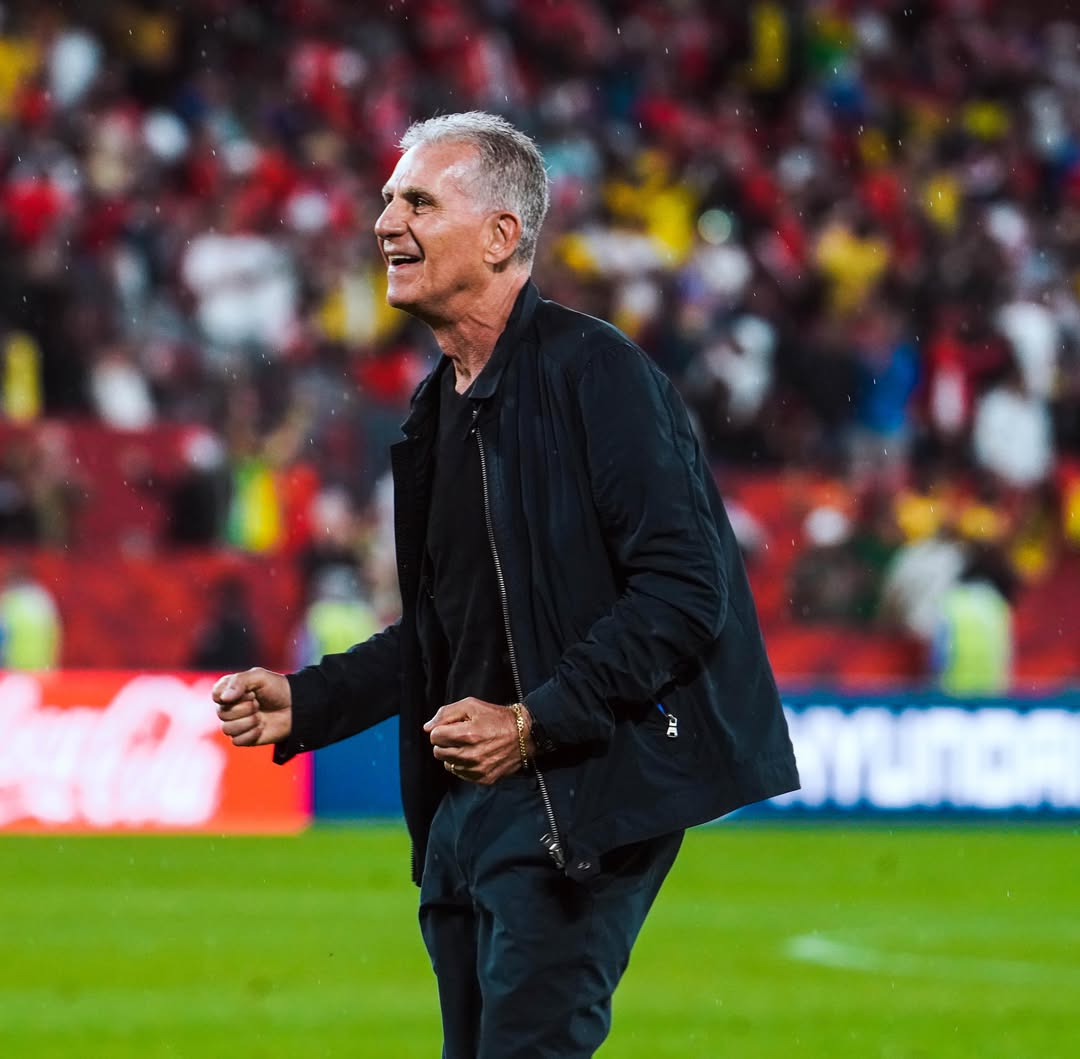 Ghana head coach Carlos Queiroz smiling and pumping his fists in celebration on the touchline under the stadium lights in rainy Toronto.