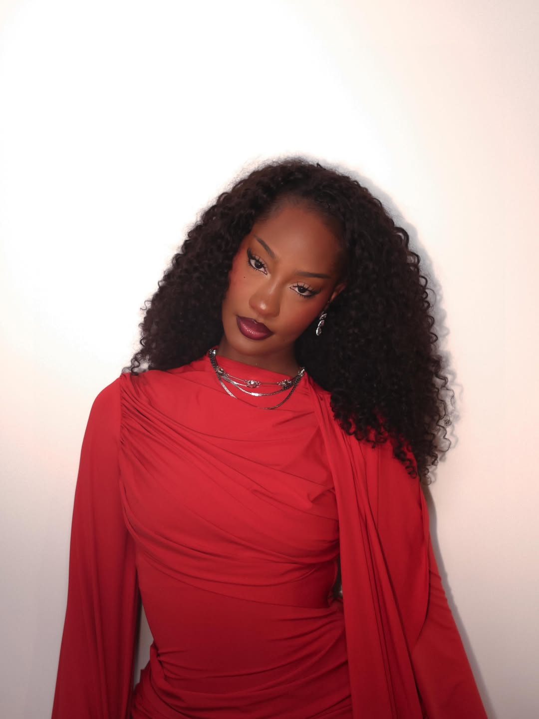 Grammy-winning artist Tems highlighting her layered silver jewelry and rich red dress chosen for her high-profile performance at the John Lewis Plaza ceremony.