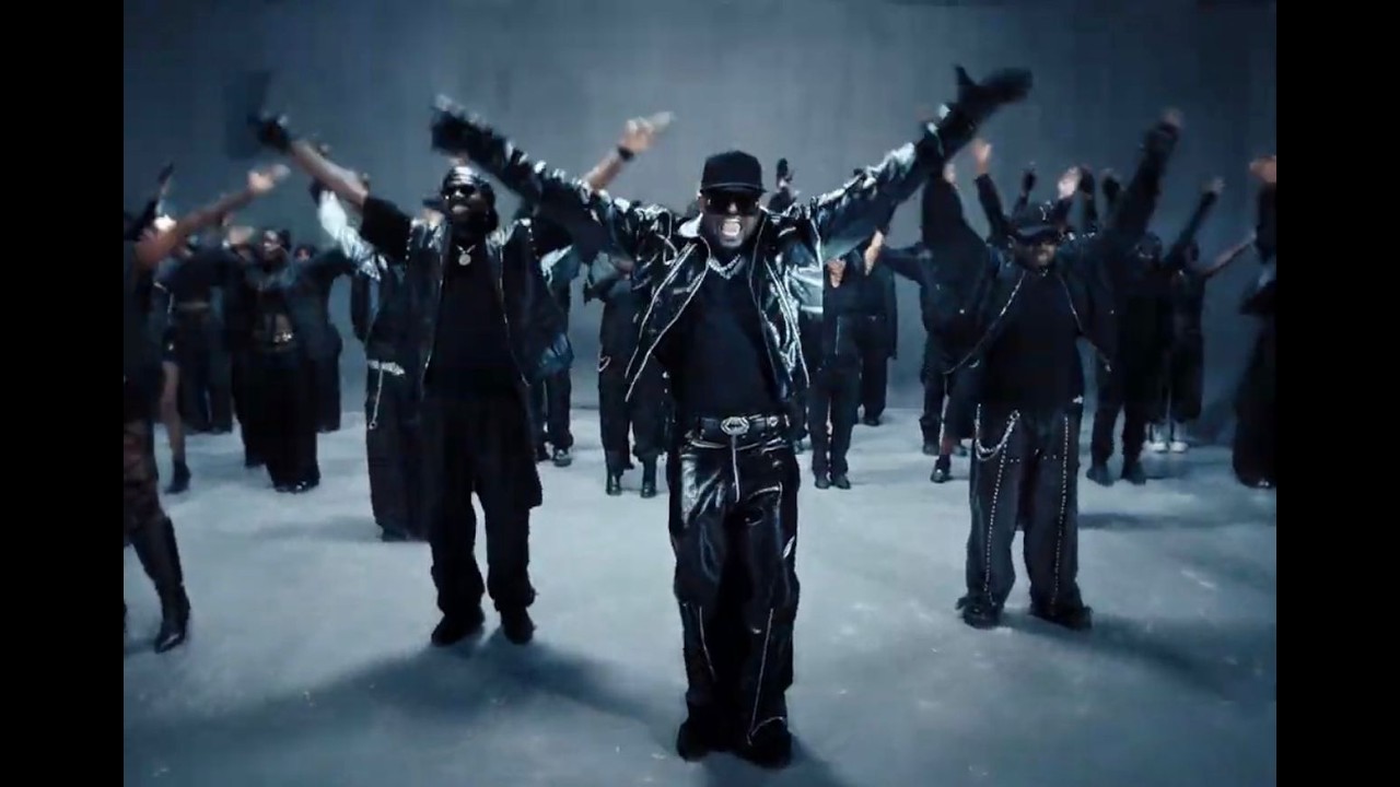 Mr P and back-up dancers dressed in matching black leather outfits performing synchronized break dance choreography.