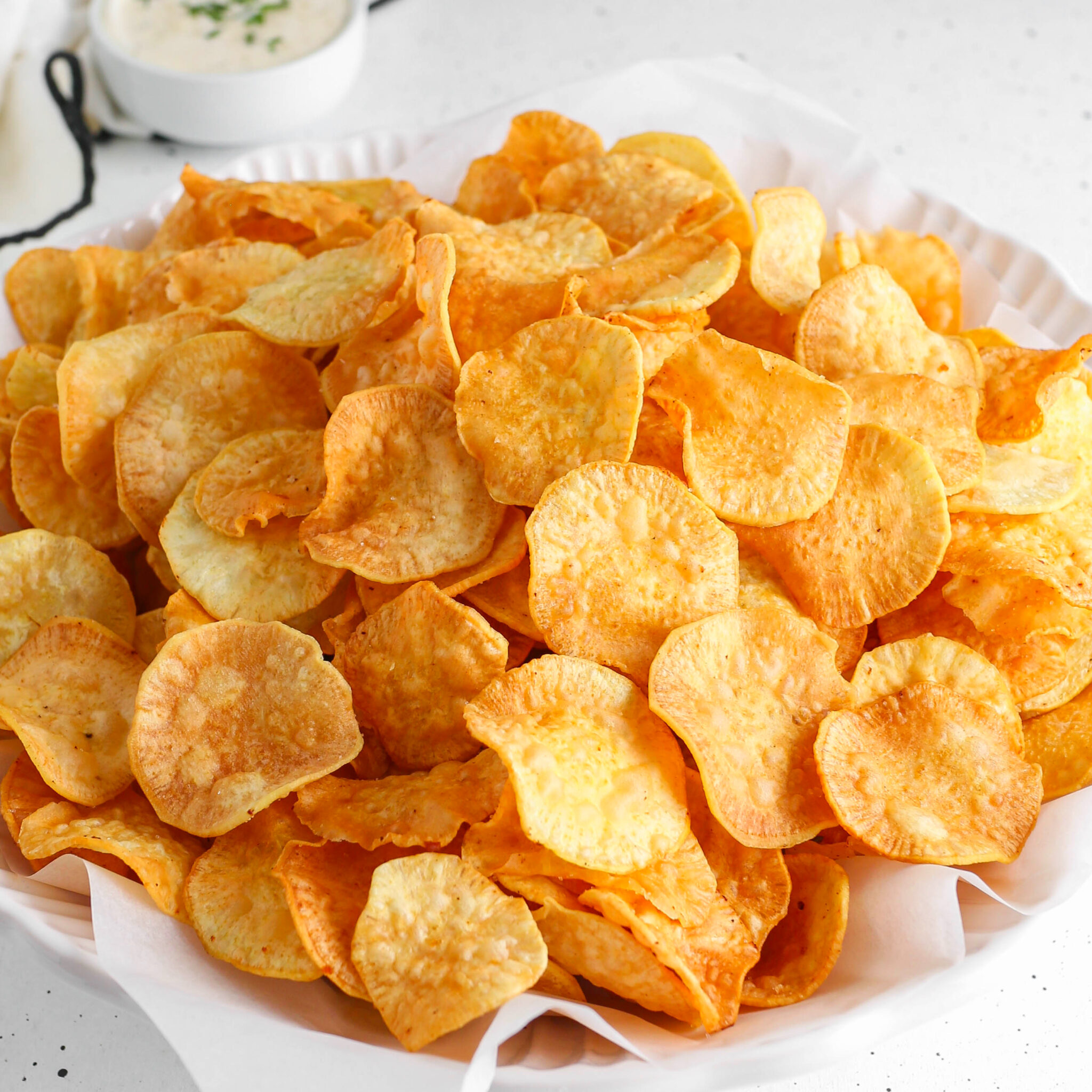 A white bowl filled with crunchy, golden-brown homemade sweet potato chips made from Nigerian white sweet potatoes, served with a side dip.
