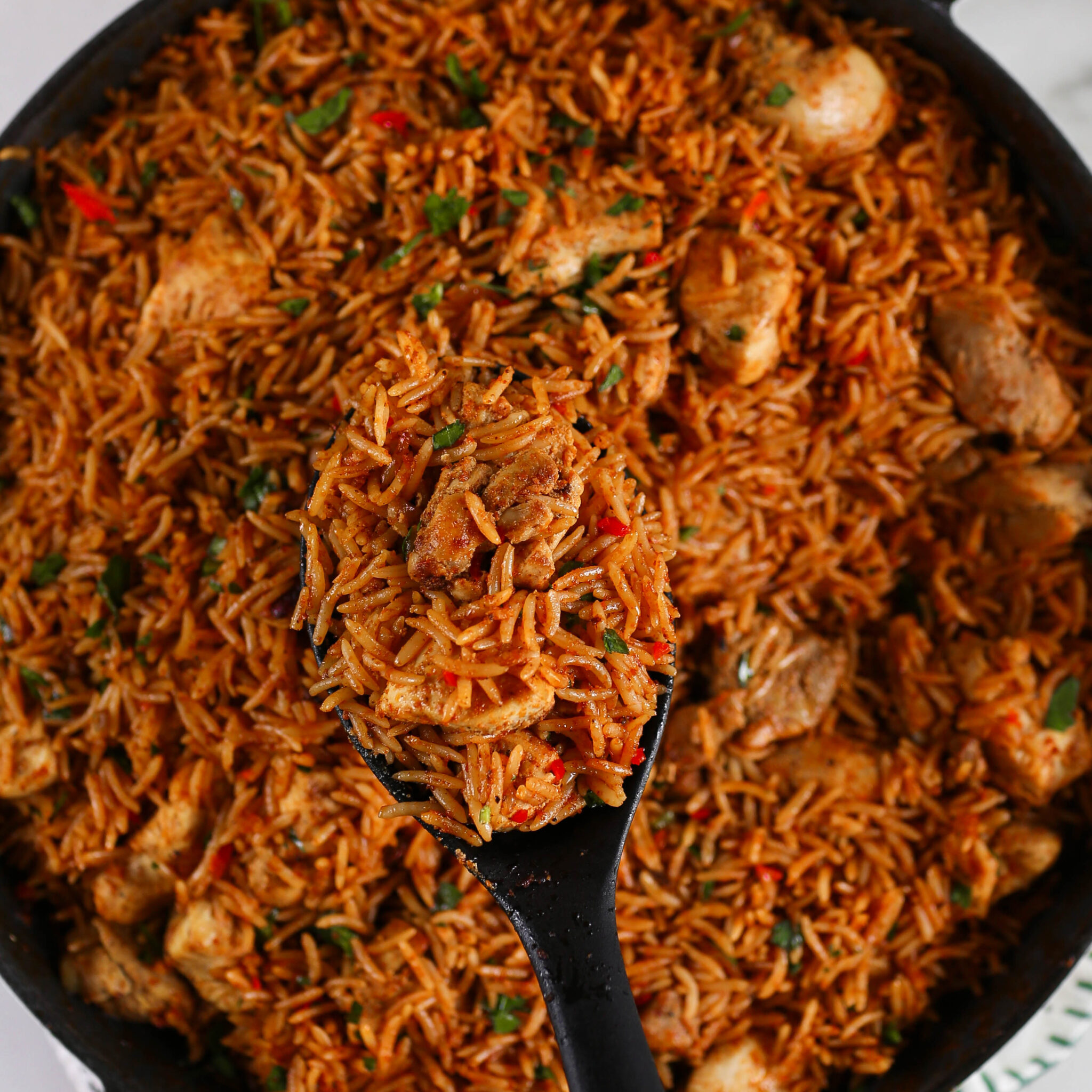 A spoon scoops up a serving of fluffy basmati rice and marinated chicken pieces from a large pot.