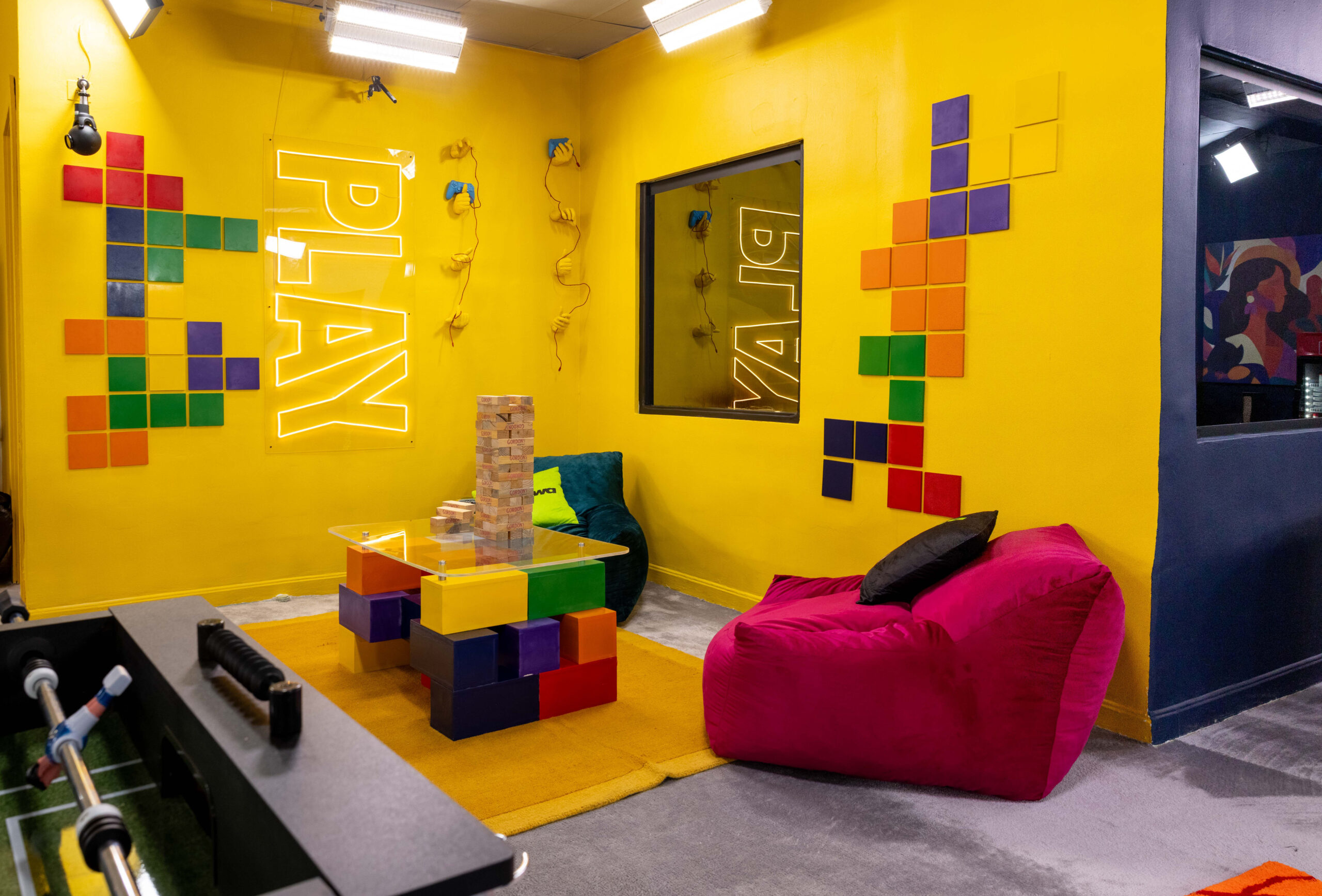 Yellow games room in the Big Brother Naija Season 11 house featuring a Foosball table, giant Jenga, and yellow PLAY neon wall sign