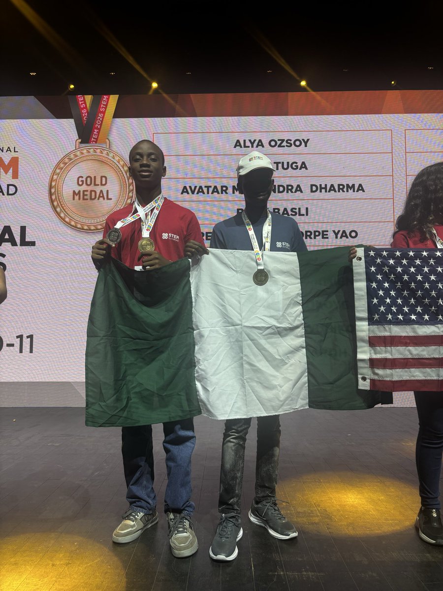Chimdiebube Onwubiko and Don Anele Munachimso holding the Nigerian flag on stage next to an international gold medal graphic.