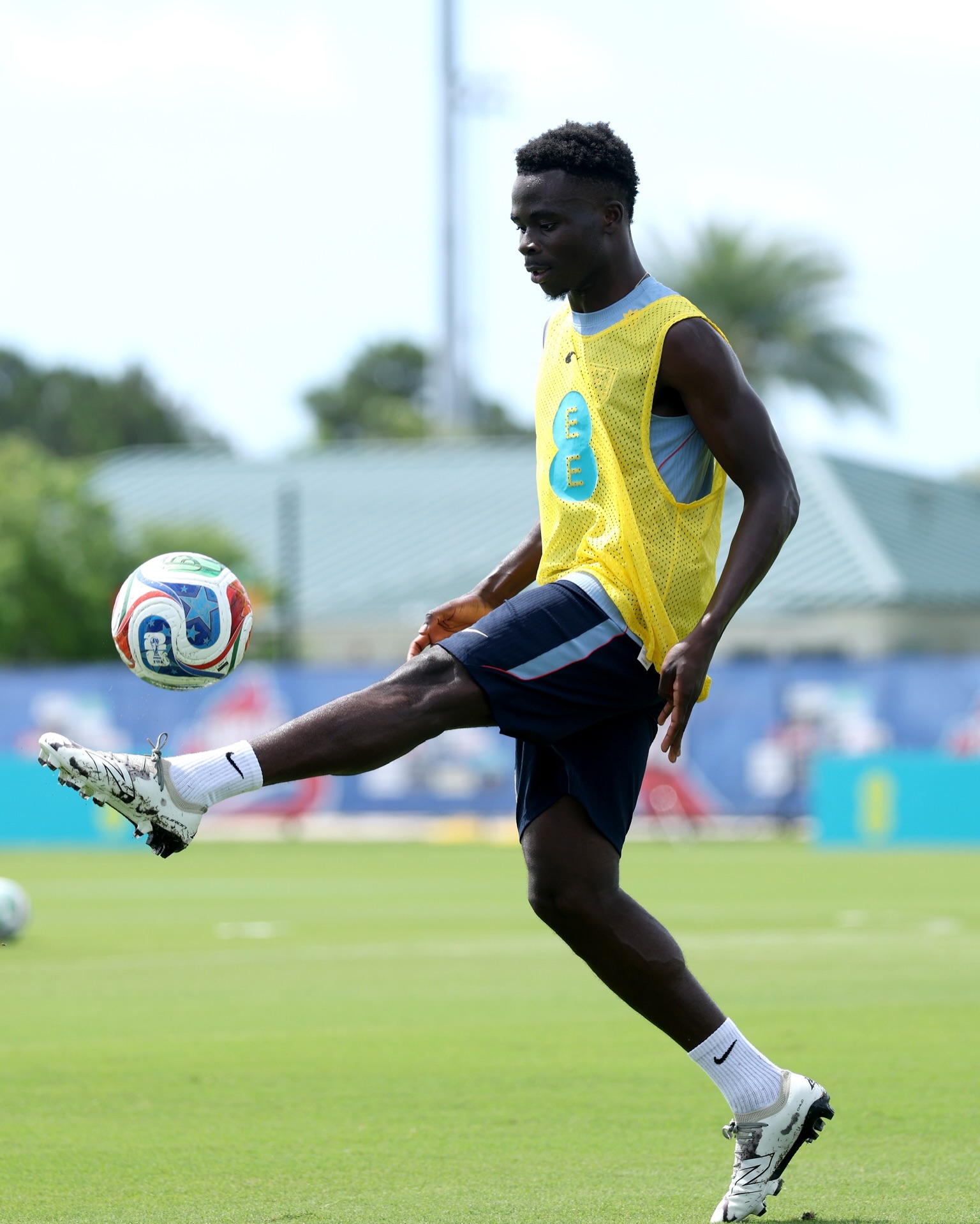 Bukayo Saka of Nigerian heritage wearing a yellow England training bib while controlling a football on a training pitch during the 2026 FIFA World Cup knockout stages.