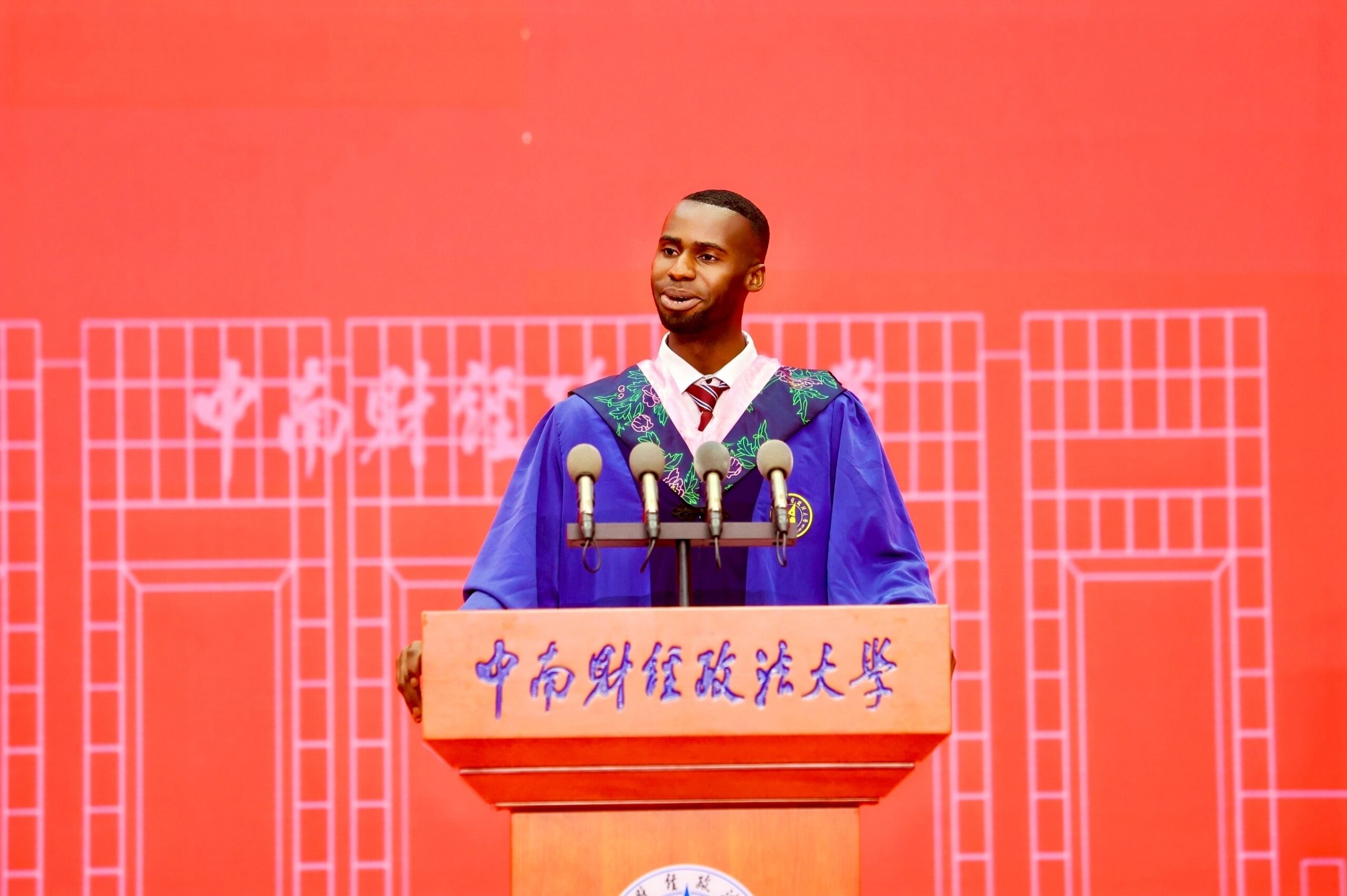 Nnabuike Chisom speaking into microphones at a wooden lectern with Chinese characters at Zhongnan University.