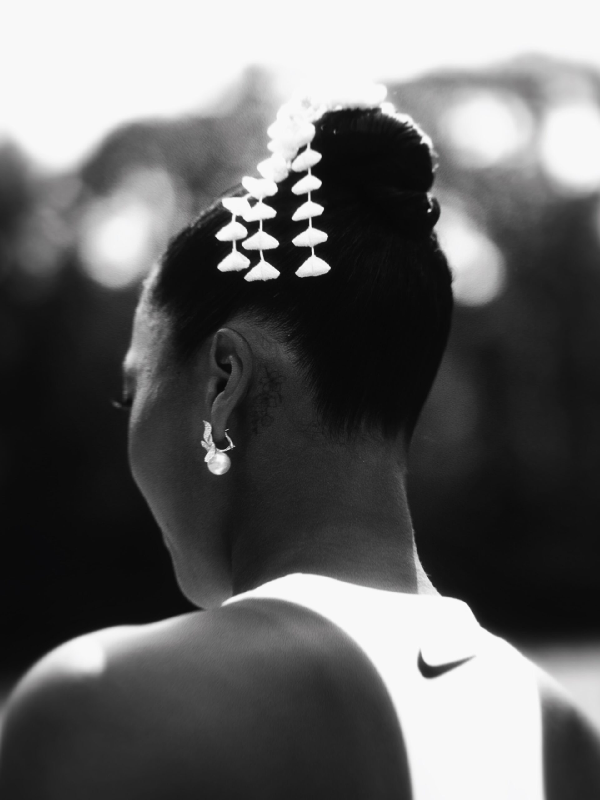 Black and white close-up of the back of Naomi Osaka's head showing a kanzashi floral hair ornament and a Mikimoto pearl earring.