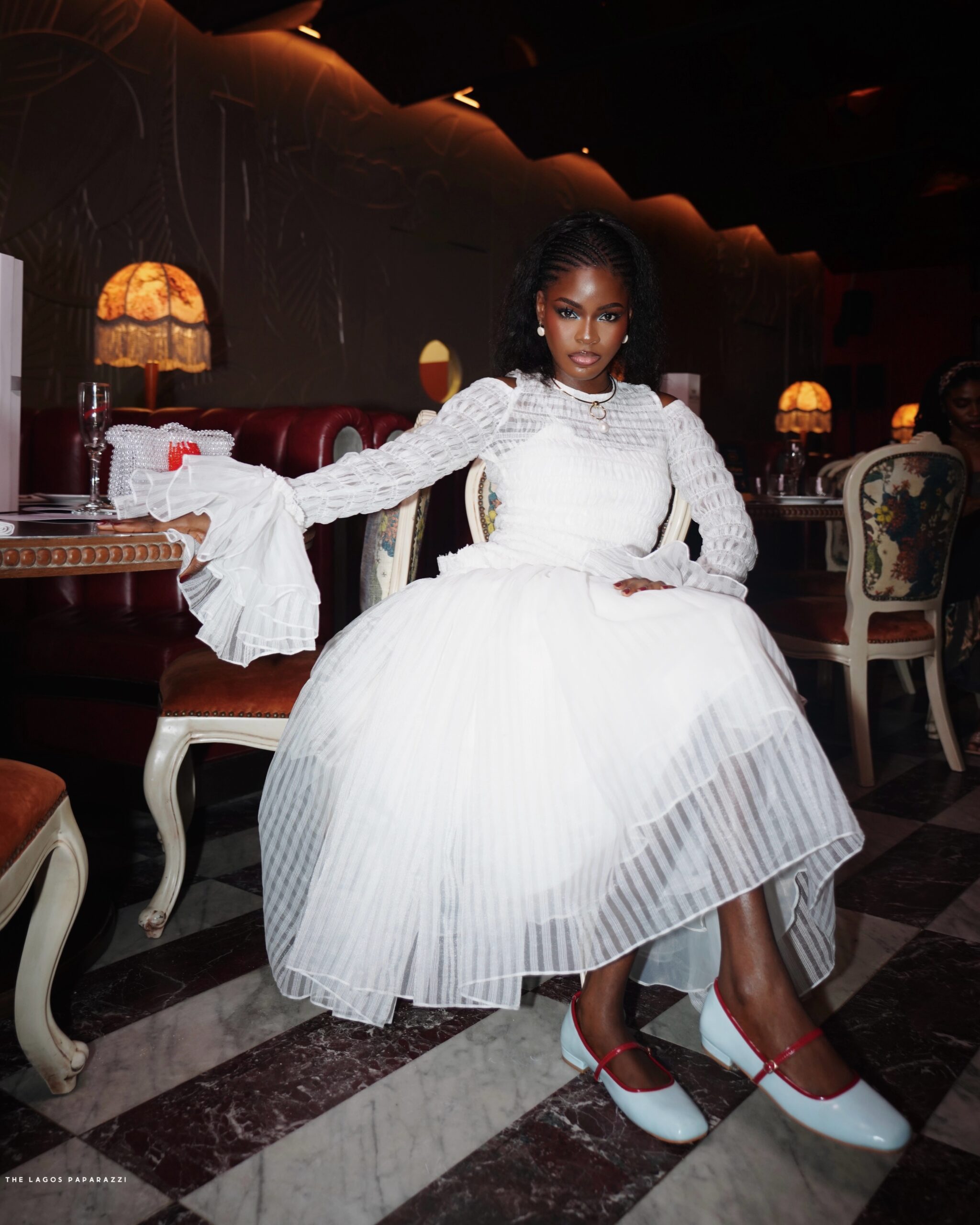 Nigerian director Korty EO wearing an elegant white tulle dress and light blue Mary Jane shoes at a restaurant in Lagos.