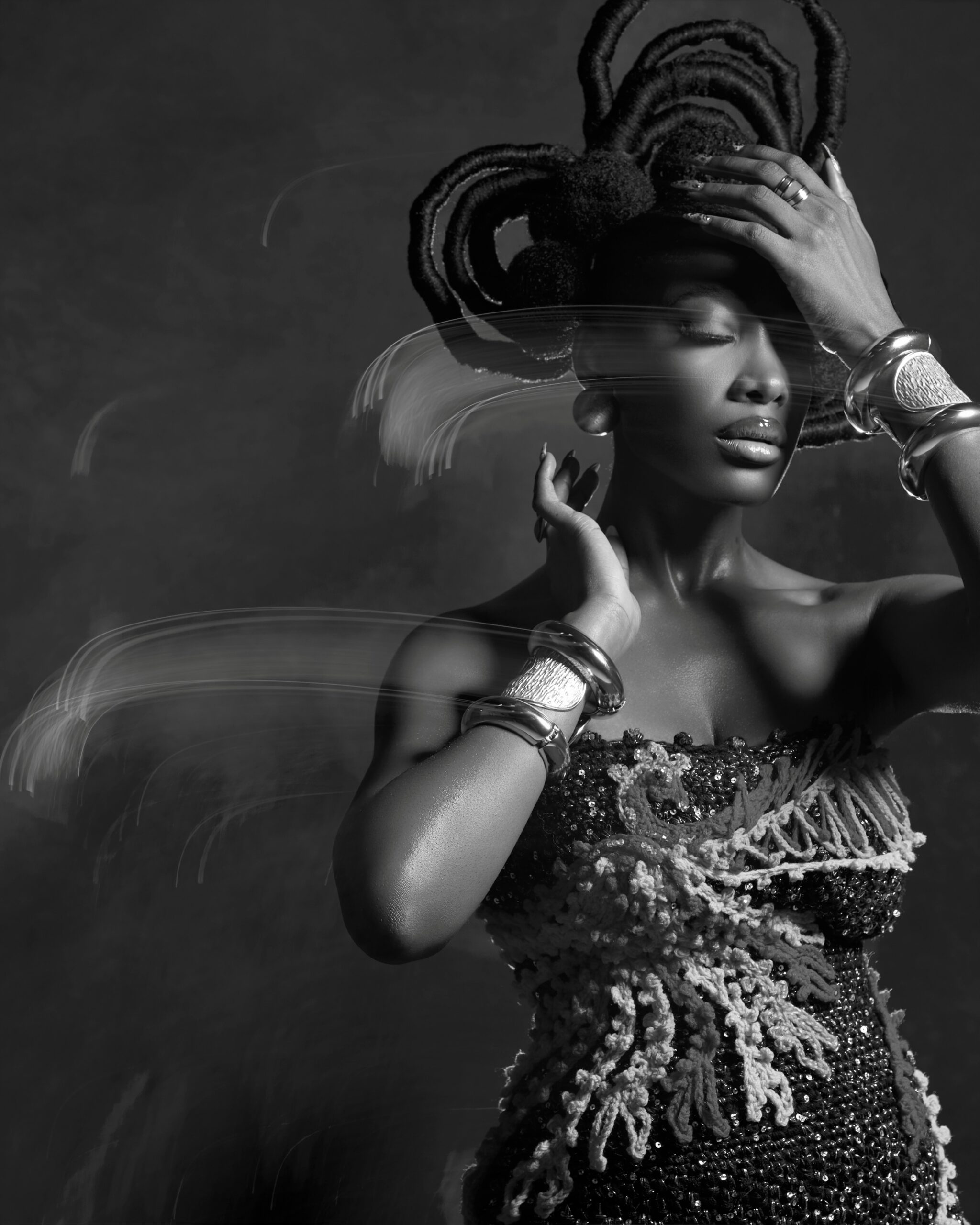 Gbubemi Ejeye in a monochrome portrait posing with silver statement cuffs and a structured thread-wrapped natural hairstyle featuring a tiered halo arch design.