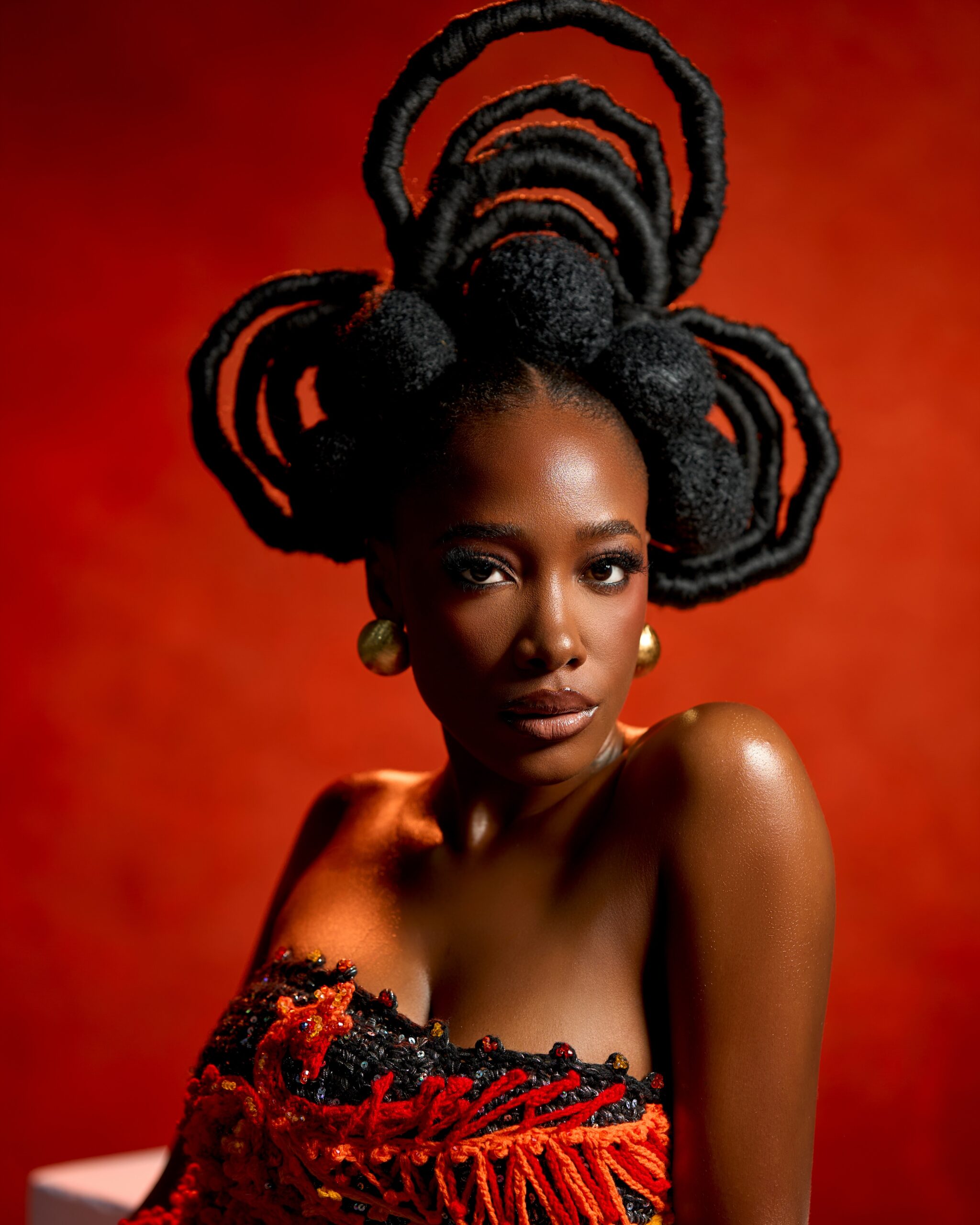 Gbubemi Ejeye looking directly at the camera wearing a structural natural hair creation made of large thread-wrapped loops and soft afro puffs.