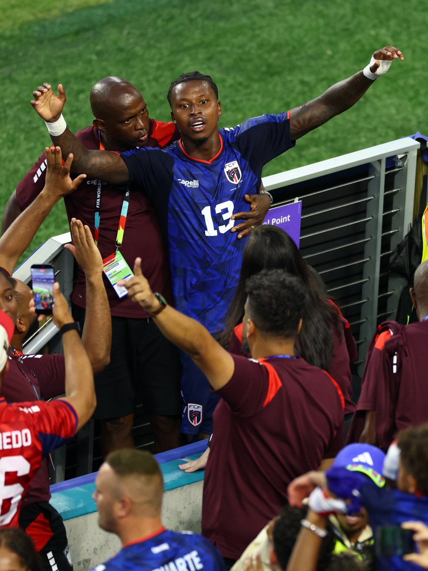 Cabo Verde player Sidny Lopes Cabral wearing the number 13 jersey celebrating near the stadium railings with fans and team staff.