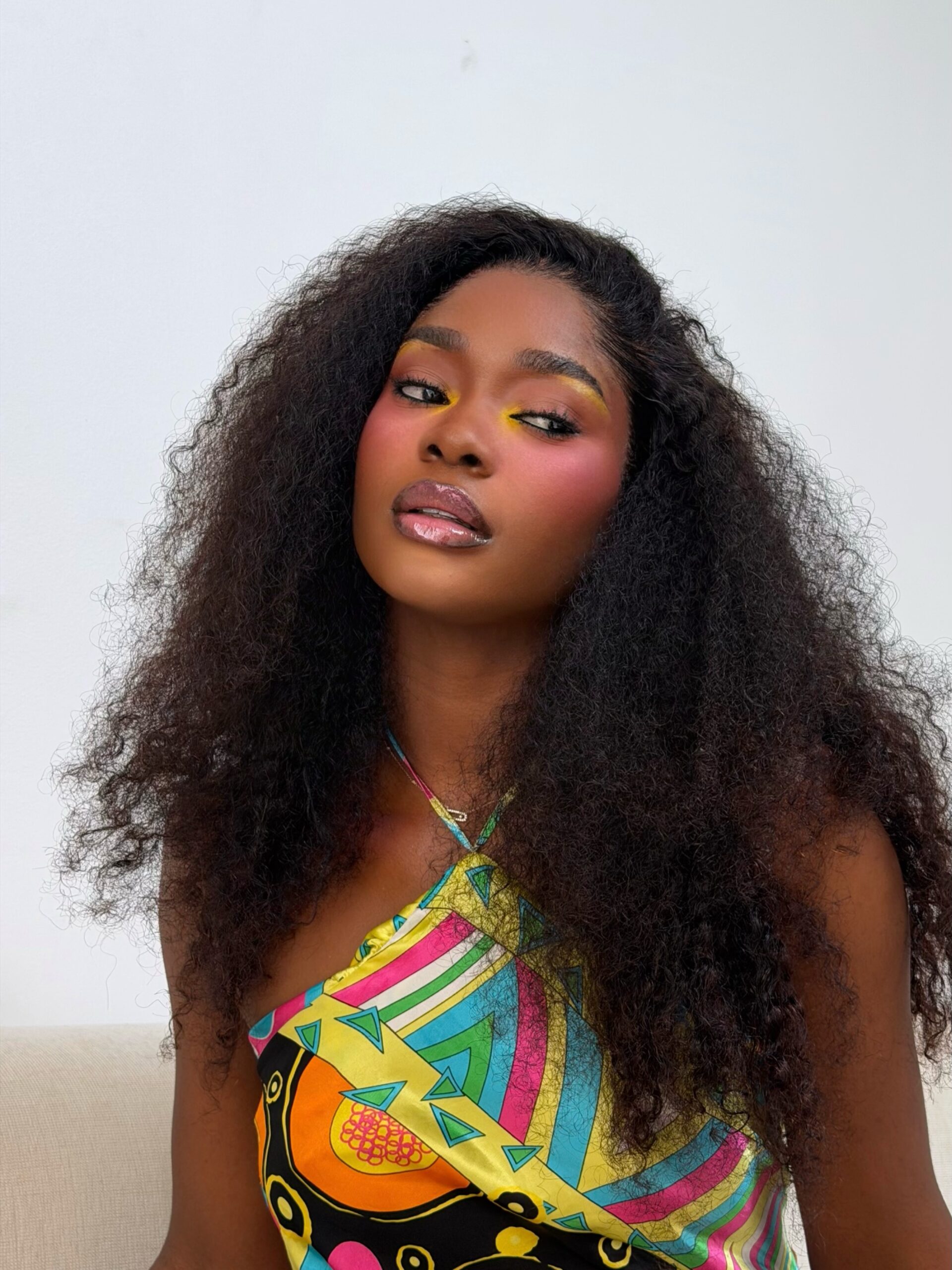 Dede Ashiogwu wears bright yellow and orange eyeshadow with black eyeliner and high-placed rose blush.