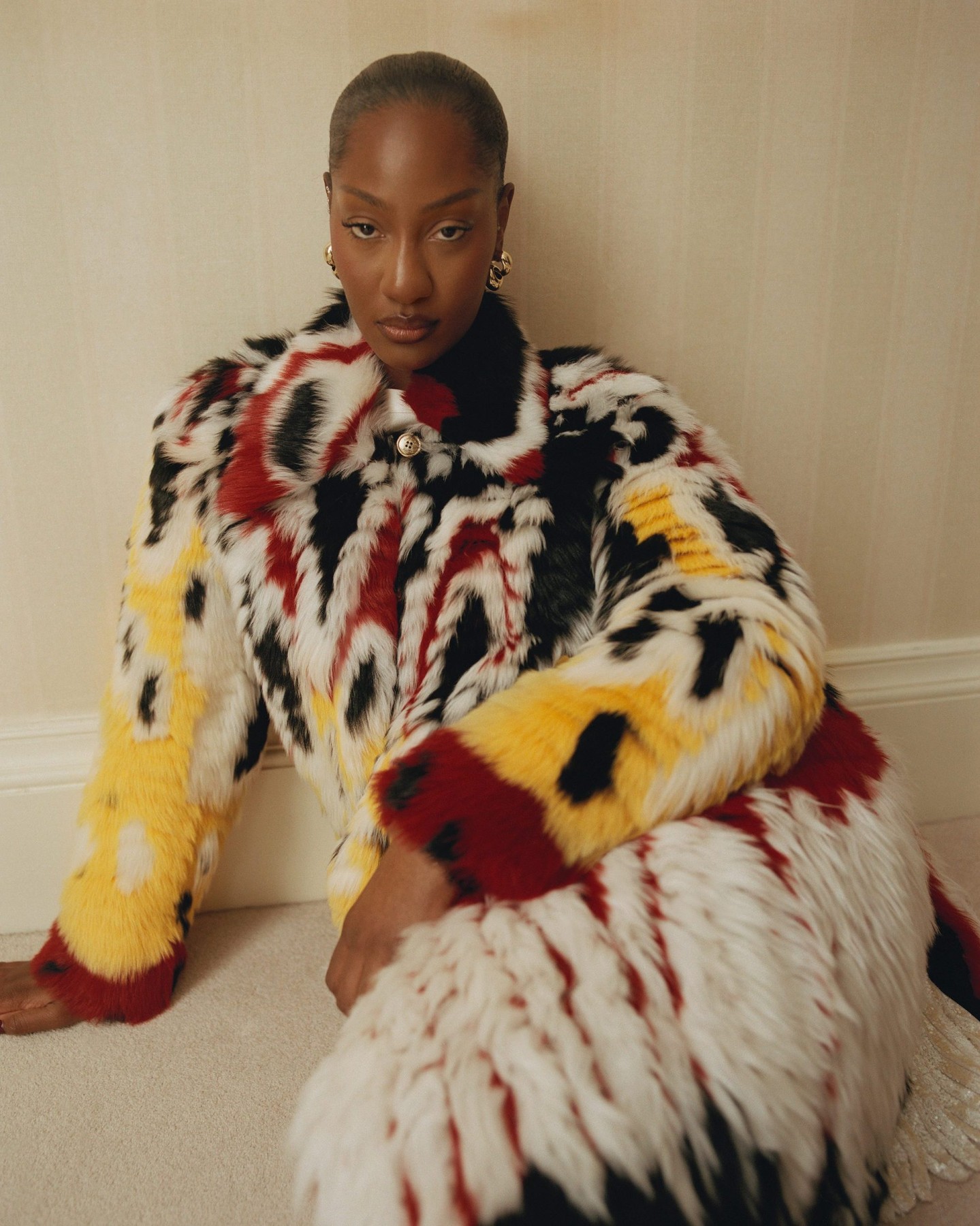 Tems wearing a patterned black, white, red, and yellow Chanel patchwork lambskin coat with gold LO Collections x Alex & Trahanas hoop earrings.