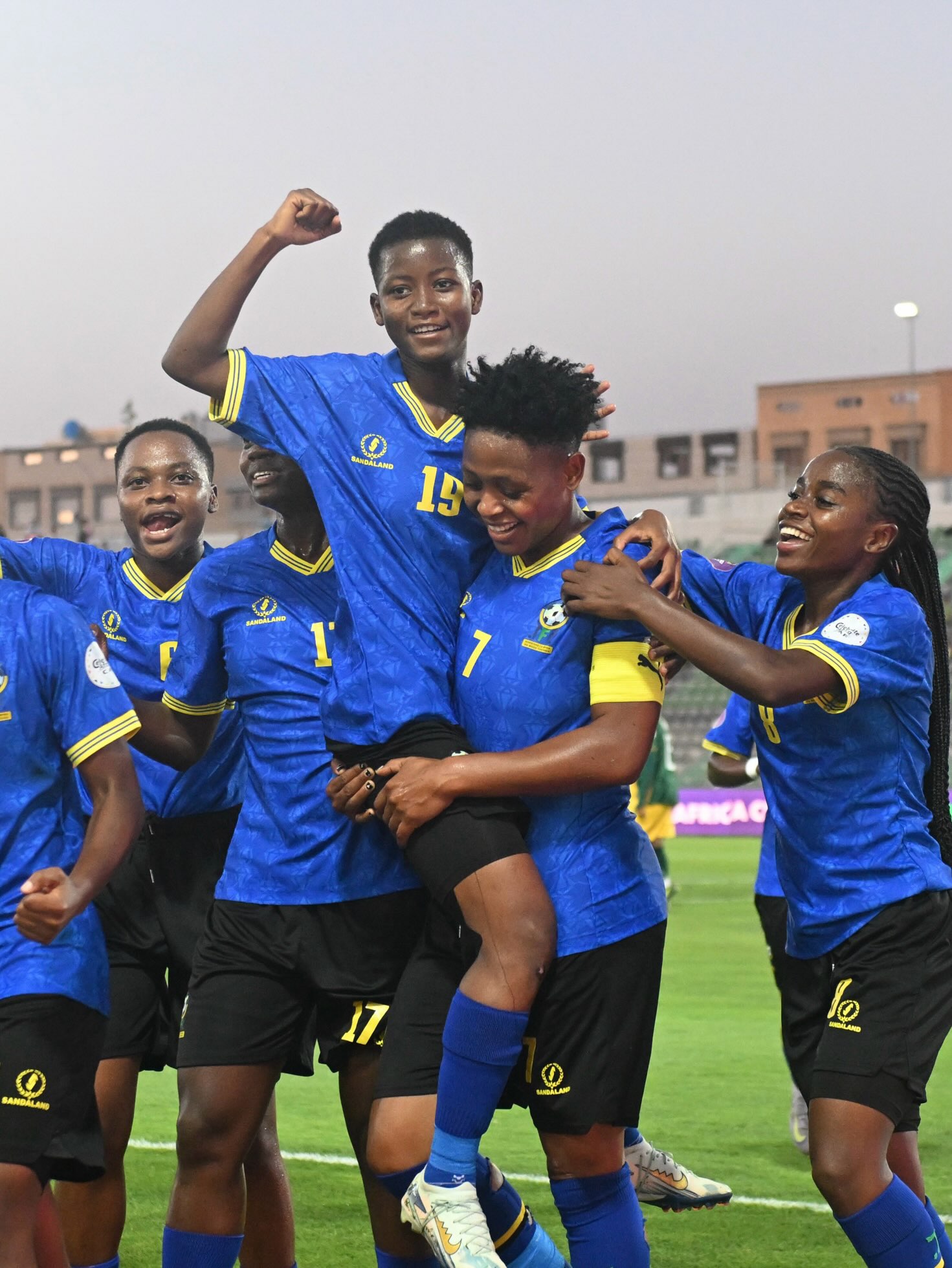 Tanzania women's national football team players celebrating on the pitch in their blue and yellow match kits.