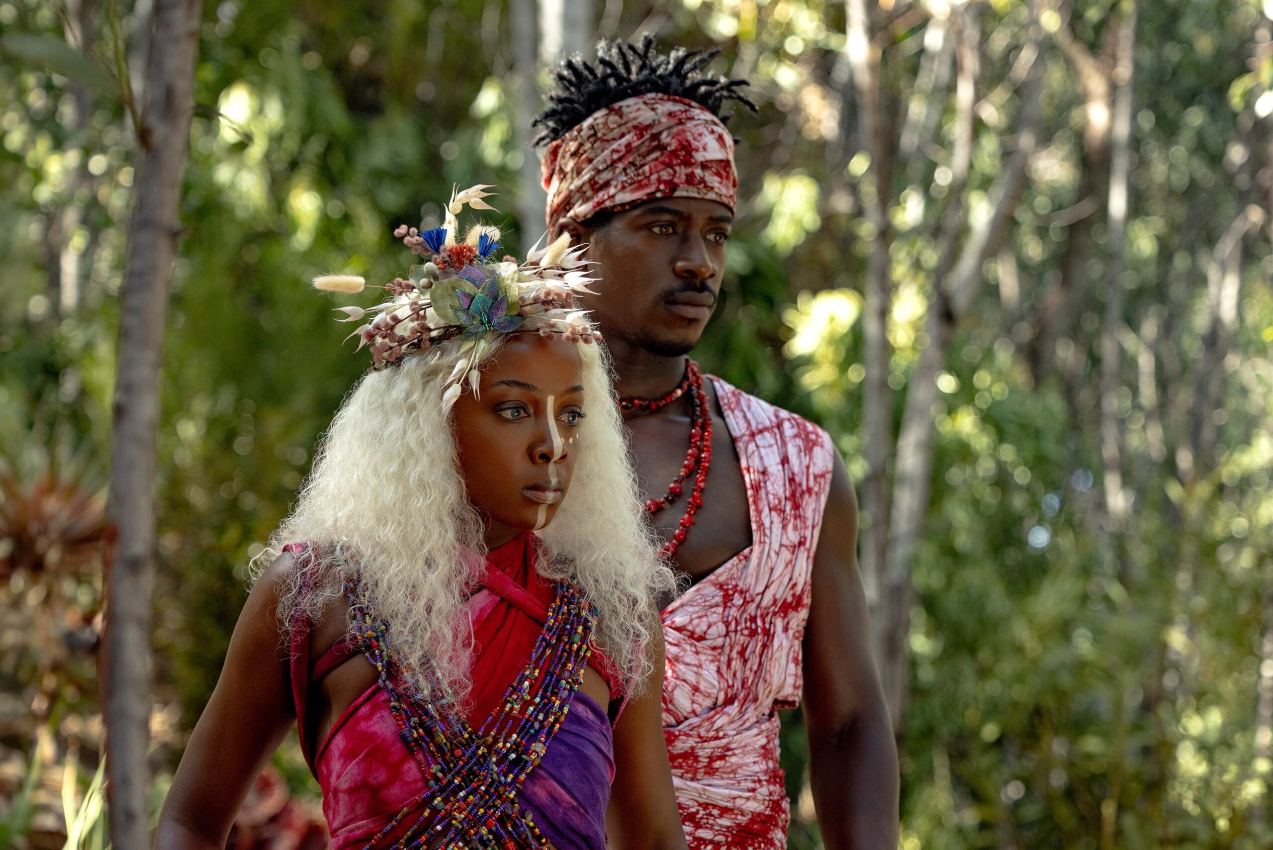 Thuso Mbedu as Zélie Adebola with white hair and a floral headpiece standing beside Damson Idris as Prince Inan in an Orïsha forest.