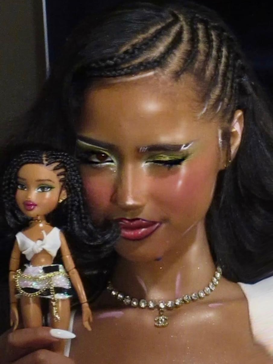 Tyla posing next to her official Bratz Celebrity Collector doll wearing matching braided hairstyle and metallic green eye makeup.