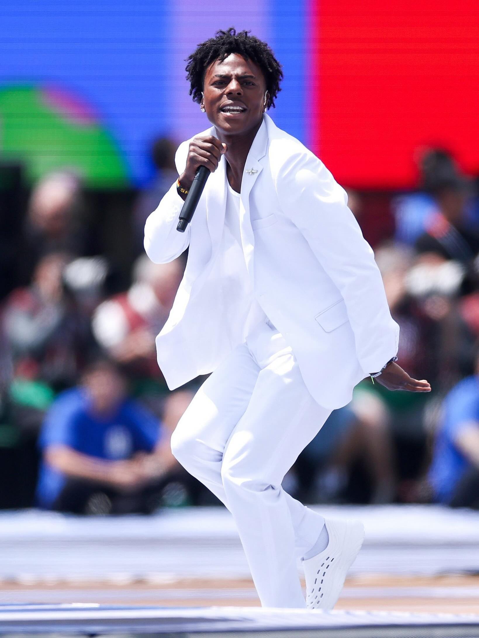 IShowSpeed dancing and singing into a microphone in an all-white suit on stage.