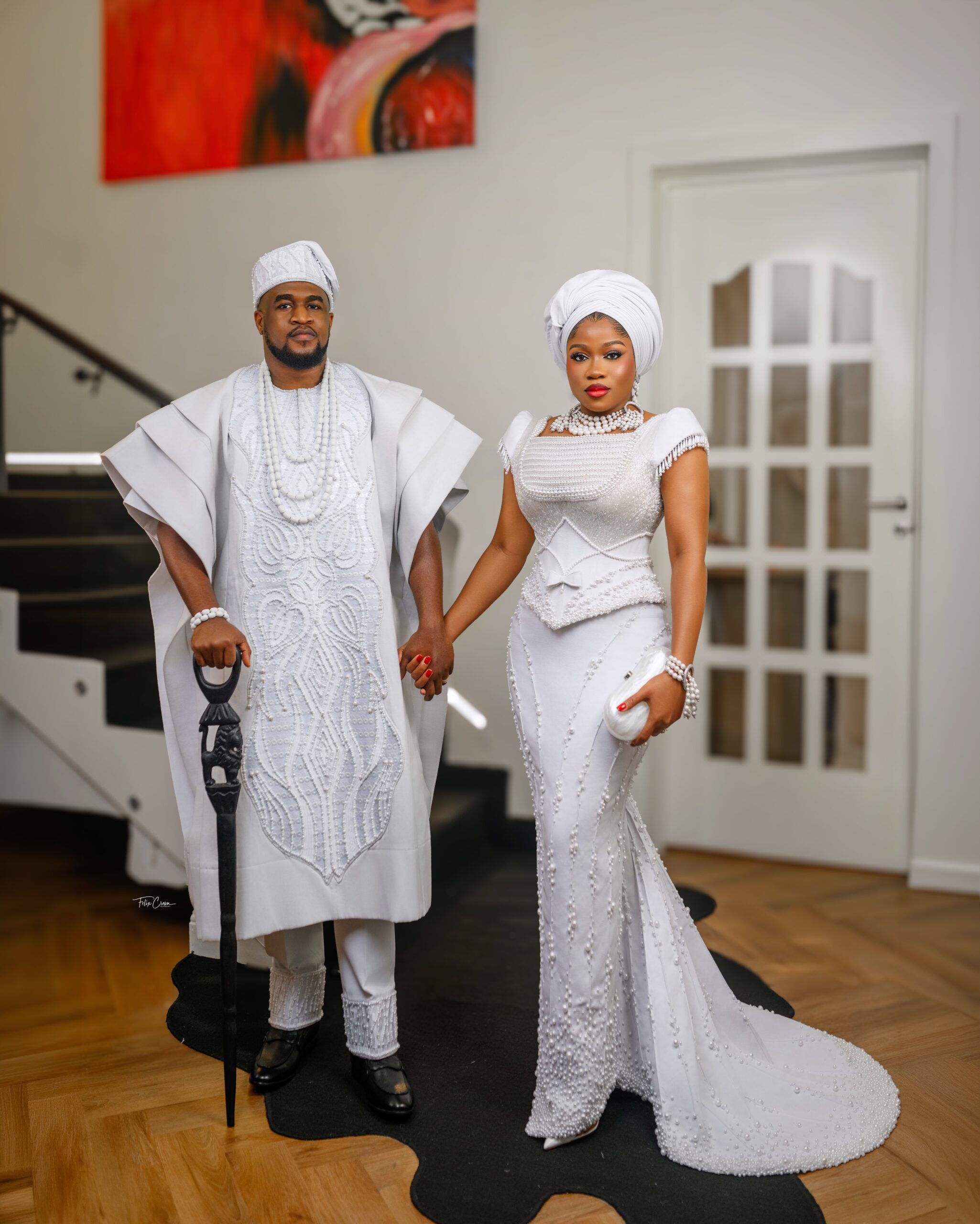 Veekee James in a pearl gown holding hands with husband Femi Atere wearing a white structured Agbada with carved lion walking stick for Eliana’s dedication.