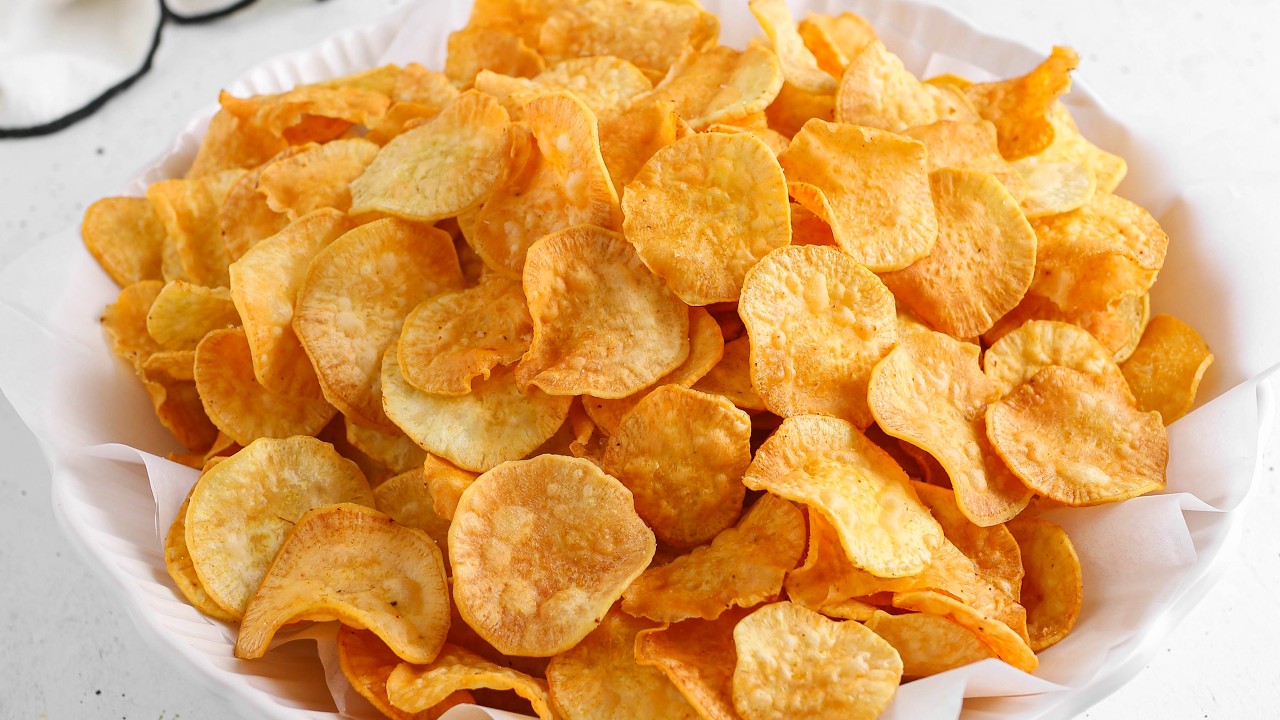 Crisp, thinly sliced fried white sweet potato chips seasoned with salt, served in a paper-lined bowl.