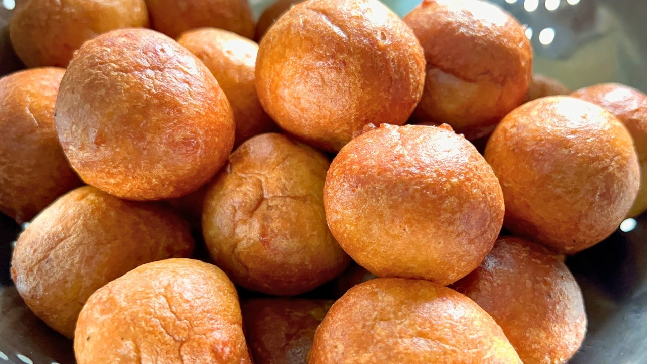 Freshly fried, golden brown, perfectly round Nigerian puff-puff balls in a colander.